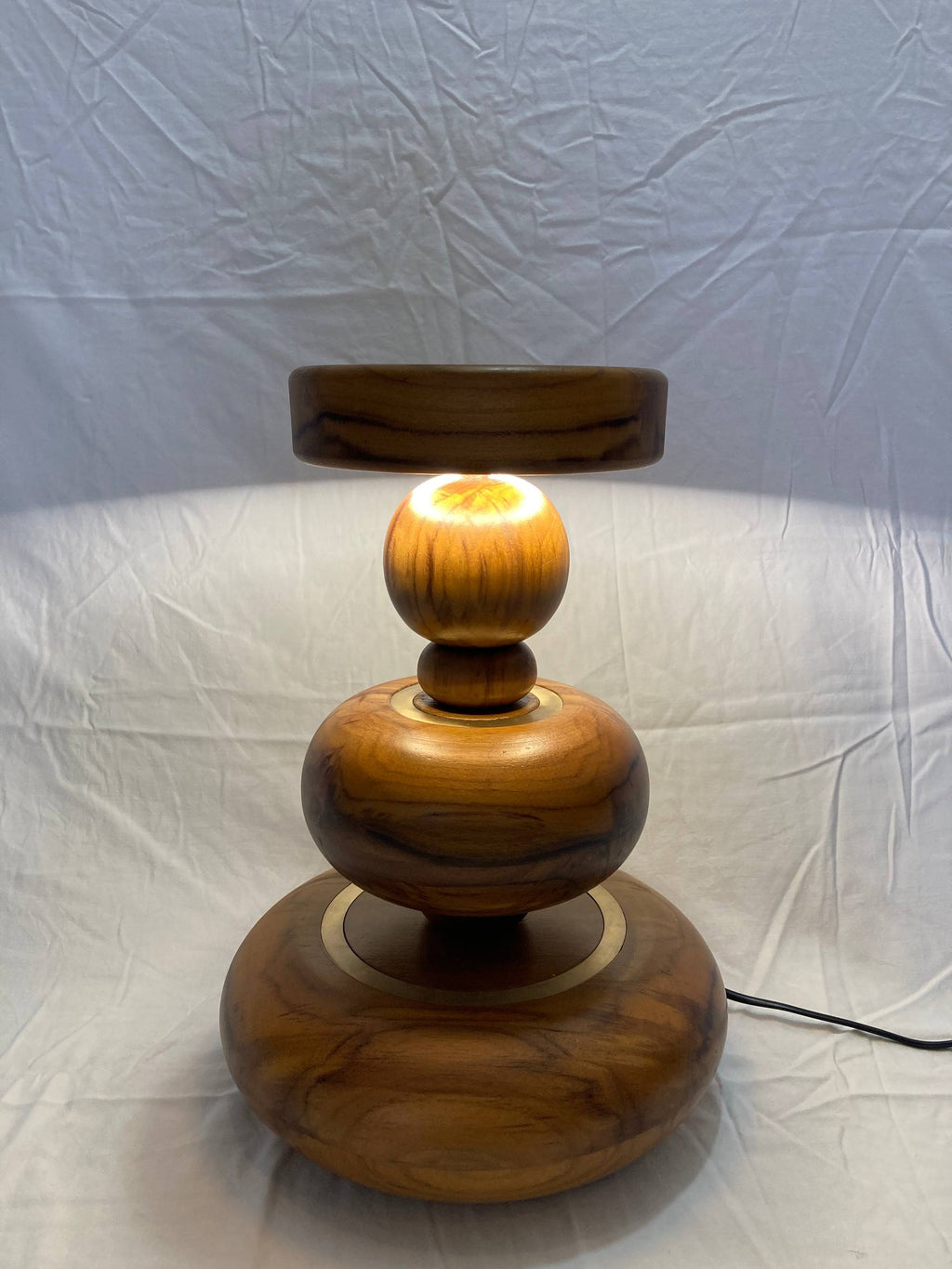 Wooden lamp with a warm glow on a white background - aikya table lamp by advit design lab - made of teak wood and brass rings